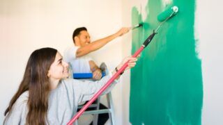 Thrilled young woman and man painting happily the walls of their new bedroom. Hispanic couple working together to paint their new home