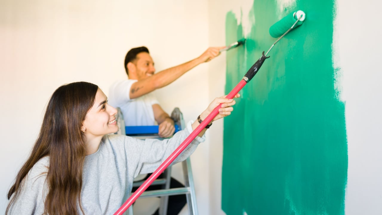 Thrilled young woman and man painting happily the walls of their new bedroom. Hispanic couple working together to paint their new home