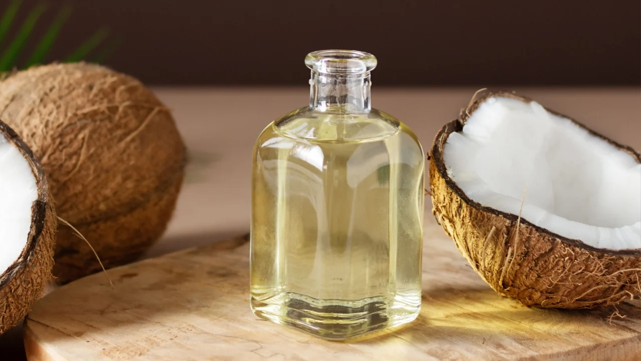 Bottle of coconut oil and fresh coconuts with palm leaf on wooden board over brown background. Coconut natural cosmetics.