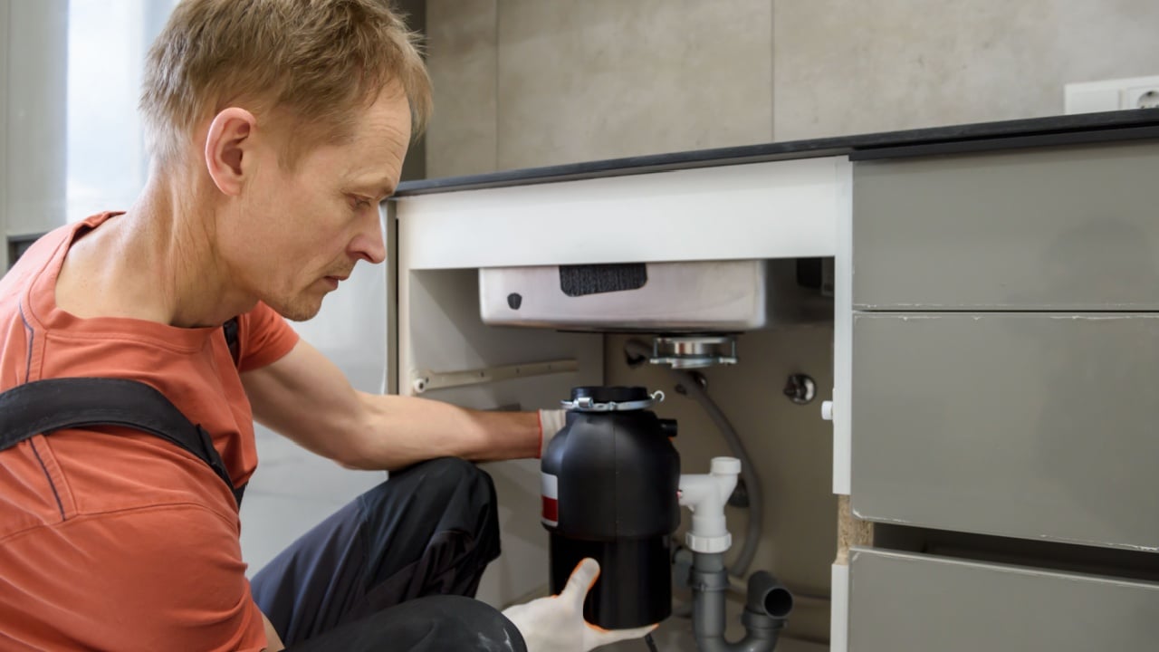 The worker is installing a household waste shredder for the kitchen sink.