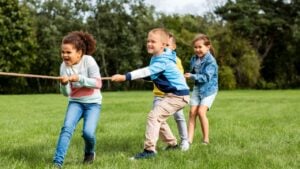 childhood, leisure and people concept - group of happy kids playing tug-of-war game and running at park