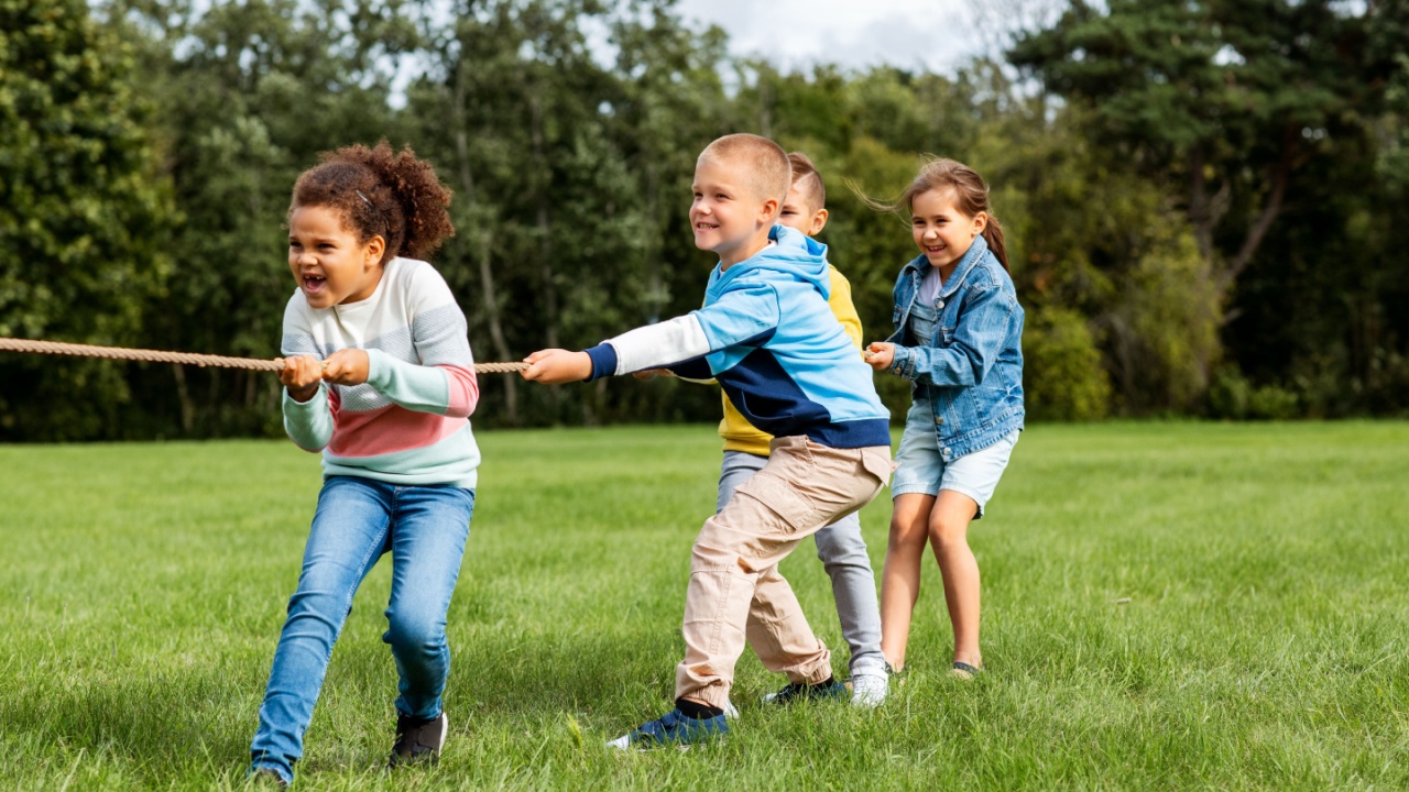 childhood, leisure and people concept - group of happy kids playing tug-of-war game and running at park