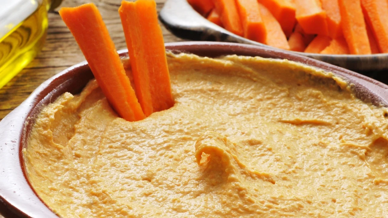 closeup of an earthenware bowl with appetizing hummus on a rustic wooden table