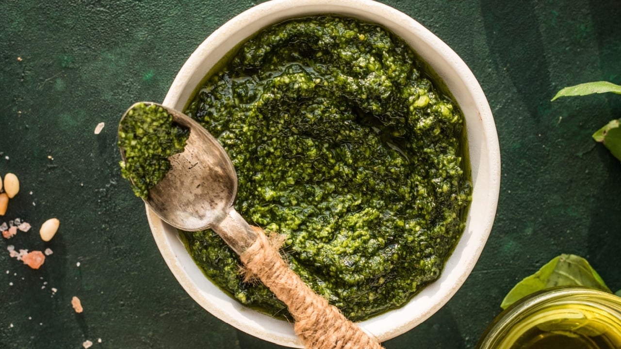 Pesto sauce in bowl with ingredients on rustic green table. Traditional Italian pesto recipe for making fettuccine, pasta, bruschetta.