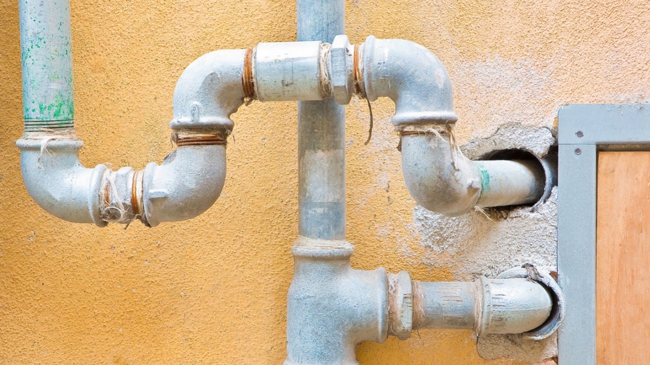 Galvanized steel metal pipes for water plumbing fixed to a brick and plaster wall with metal box for water meter 