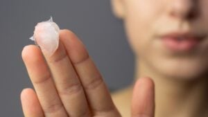 A young woman is applying petroleum jelly to her face.