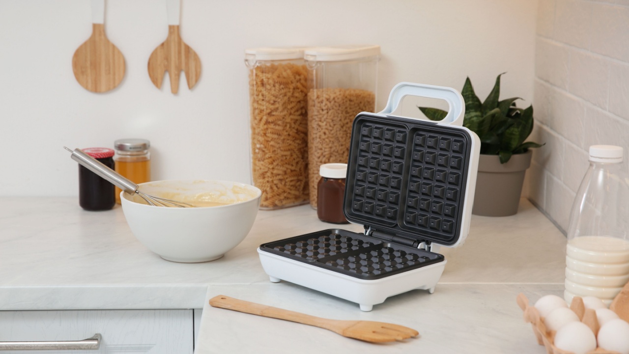 Modern electric waffle maker and ingredients on white countertop indoors