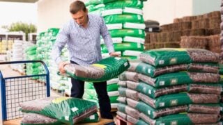 Satisfied Man choosing compost soil in plastic bags in hypermarket .