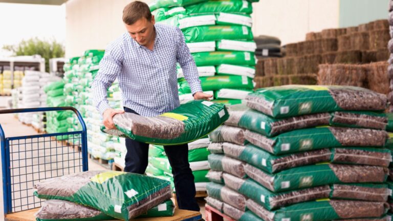 Satisfied Man choosing compost soil in plastic bags in hypermarket .