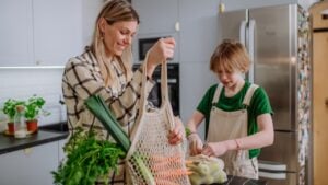 Mother unpacking local food in zero waste packaging from bag with help of daughter in kitchen at home.