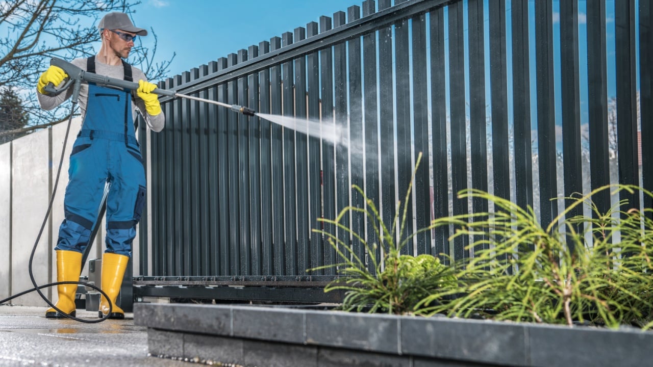Caucasian Men Washing His Residential Driveway Gate Using Pressure Washer. Home Surrounding Maintenance.