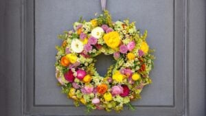 Flower wreath hanging on a house wooden door. Fresh wild flowers and herbs, home decoration, front view. Spring sunny day. Women or mothers day celebration