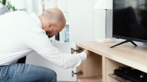 Man repairing a loose cabinet door hinge at home using a screwdriver