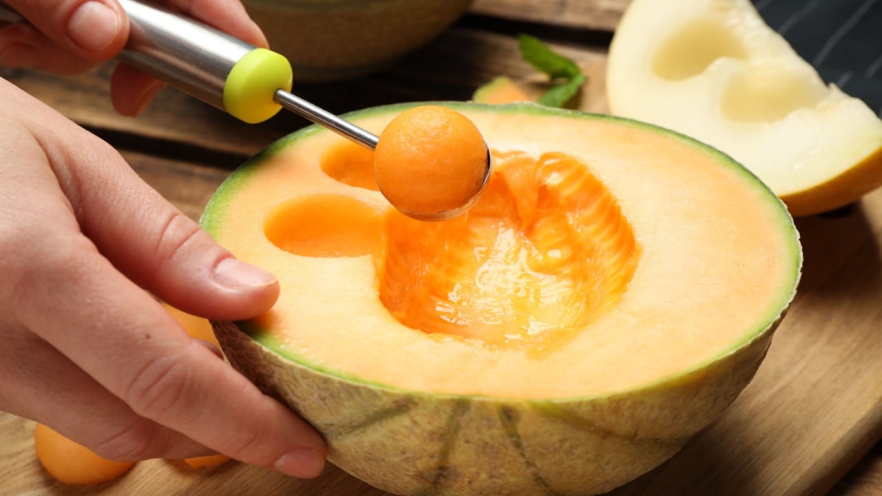 Woman making melon balls at wooden table.