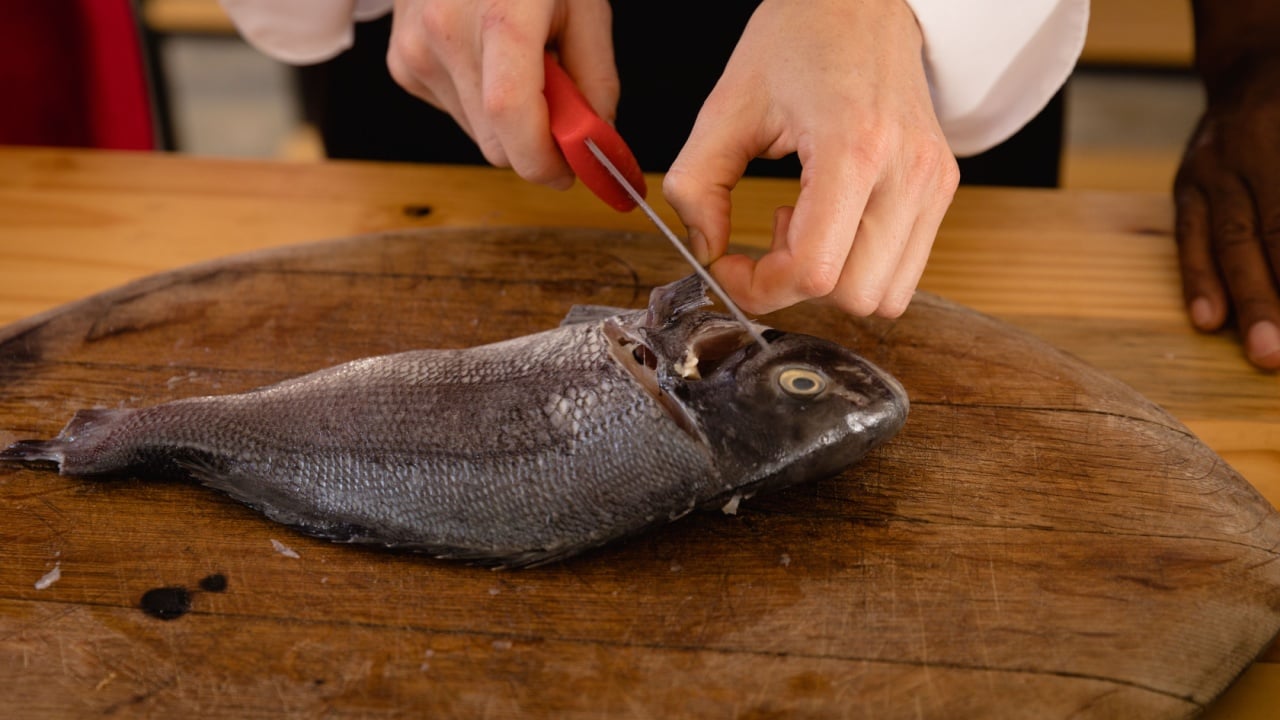 High angle view of a fish on a wooden chopping board, ready for preparation, on a wooden table in a kitchen
