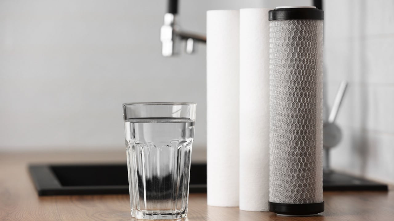 A glass of clean fresh water and set of filter cartridges on wooden table in a kitchen interior. Installation of reverse osmosis water purification system. Concept Household filtration system