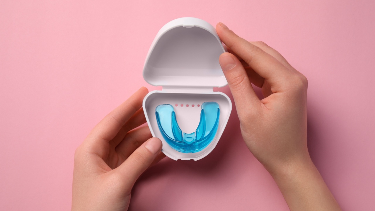 Woman holding container with mouth guard on light pink background, top view. Bite correction