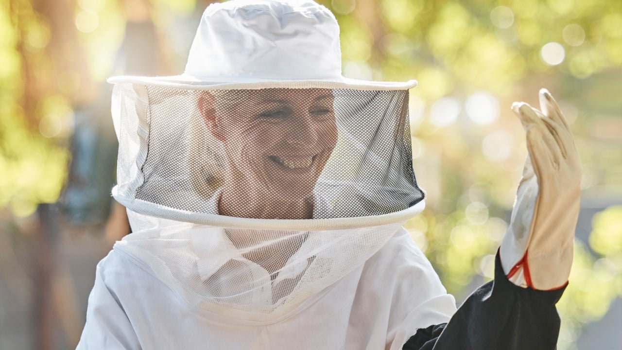 Beekeeper woman, smile and safety at farm with apiculture suit