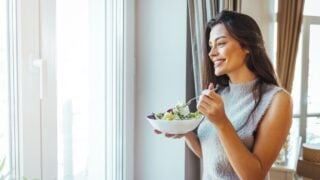 Healthy diet. Beautiful woman on the sofa eating a healthy salad. Beautiful healthy woman eating lettuce. Girl eating organic fresh salad. Close-up of a smiling woman eating a salad in the living-room