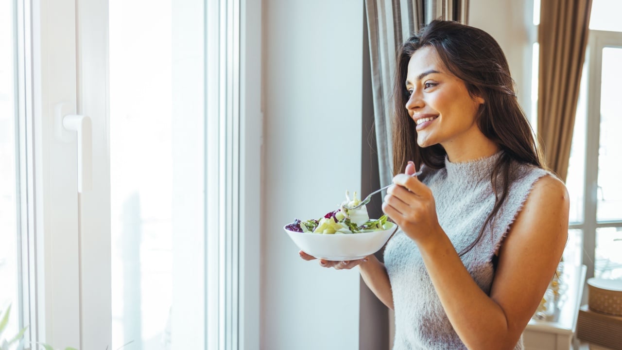 Healthy diet. Beautiful woman on the sofa eating a healthy salad. Beautiful healthy woman eating lettuce. Girl eating organic fresh salad. Close-up of a smiling woman eating a salad in the living-room