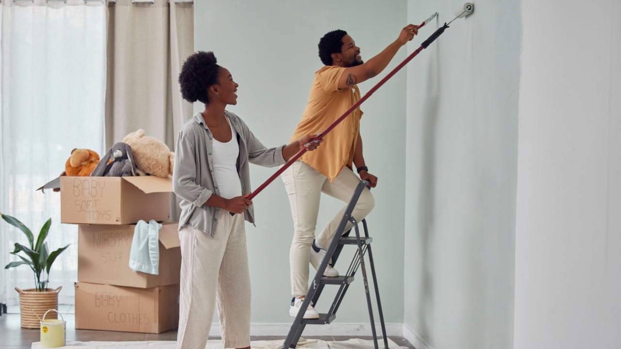 Painting, teamwork or black couple home renovation, diy or house remodel together with paintbrush or roller. Happy smile, woman and African man love working on wall with partnership or collaboration