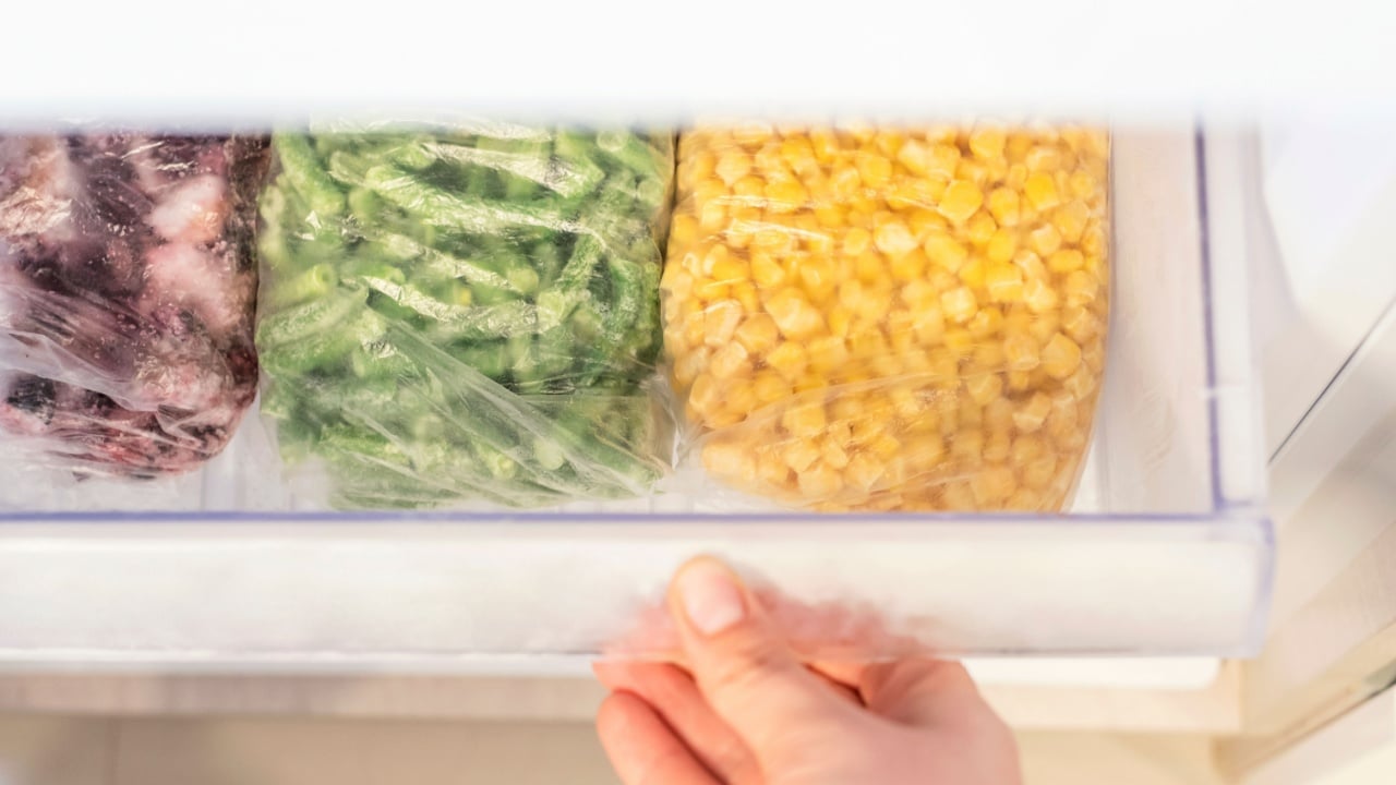 Female hand opens a shelf with frozen food in the refrigerator close up top view.