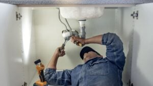 Plumber, man and handyman with plumbing, home renovation and manual labour with tools. Construction, DIY skills and professional, fixing pipe in industry and male with trade, repairs and maintenance