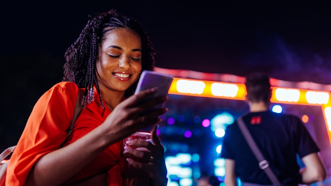 Young african american woman using a smartphone while standing in a crowd at music festival