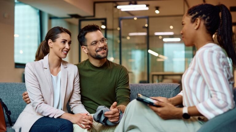 Young happy couple having a meeting with African American female insurance agent in the office.