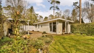 a small house in the middle of a garden with green grass and trees surrounding it is surrounded by white clouds