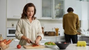 Smiling woman cutting tomatoes for healthy salad, couple cooking dinner