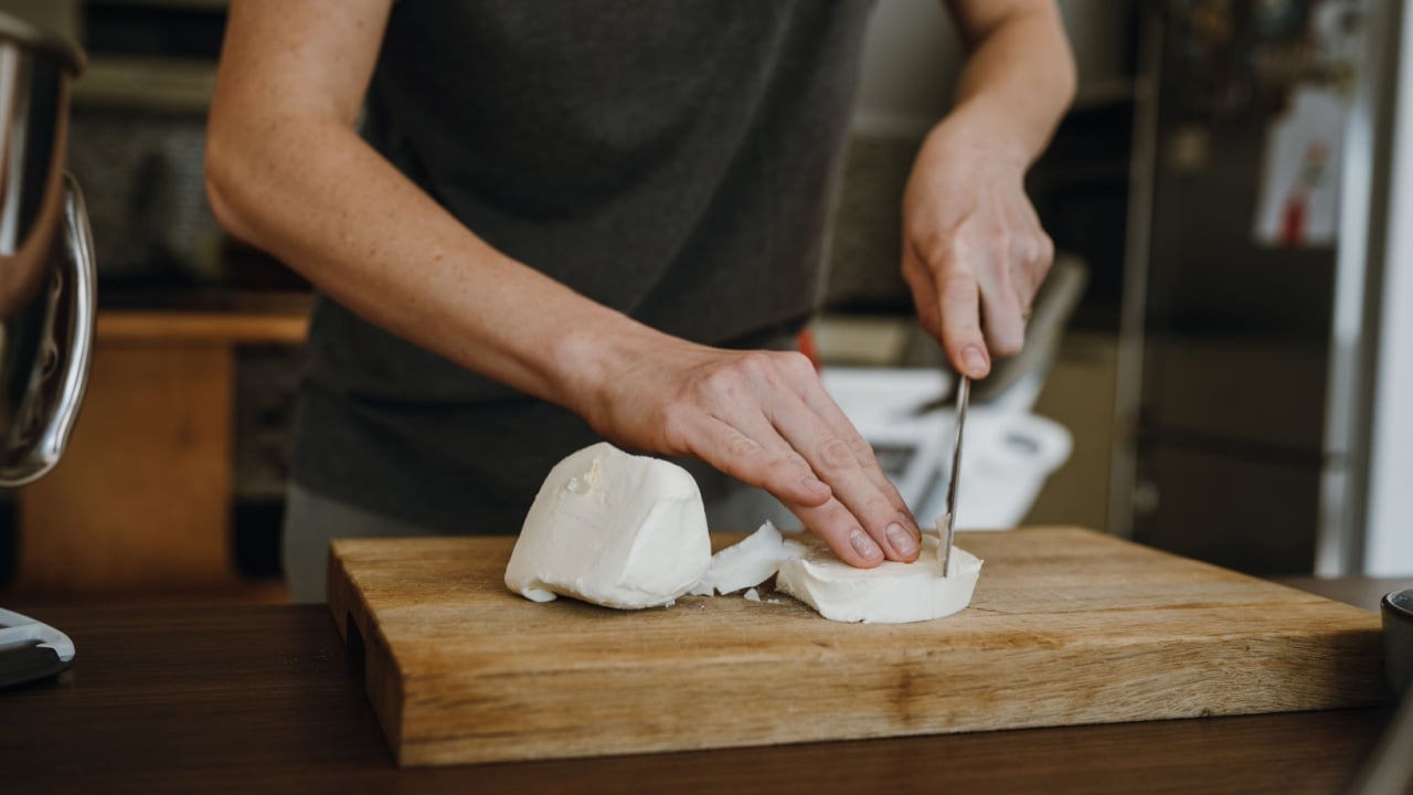 Women's hands cutting butter or white cheese with knife on wooden board. Preparing holiday dinner.