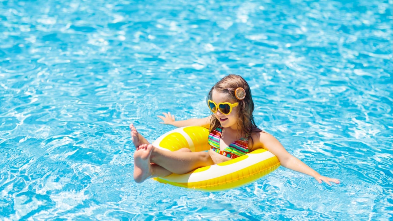 Child in swimming pool on inflatable yellow lemon ring. Little girl learning to swim with orange float.