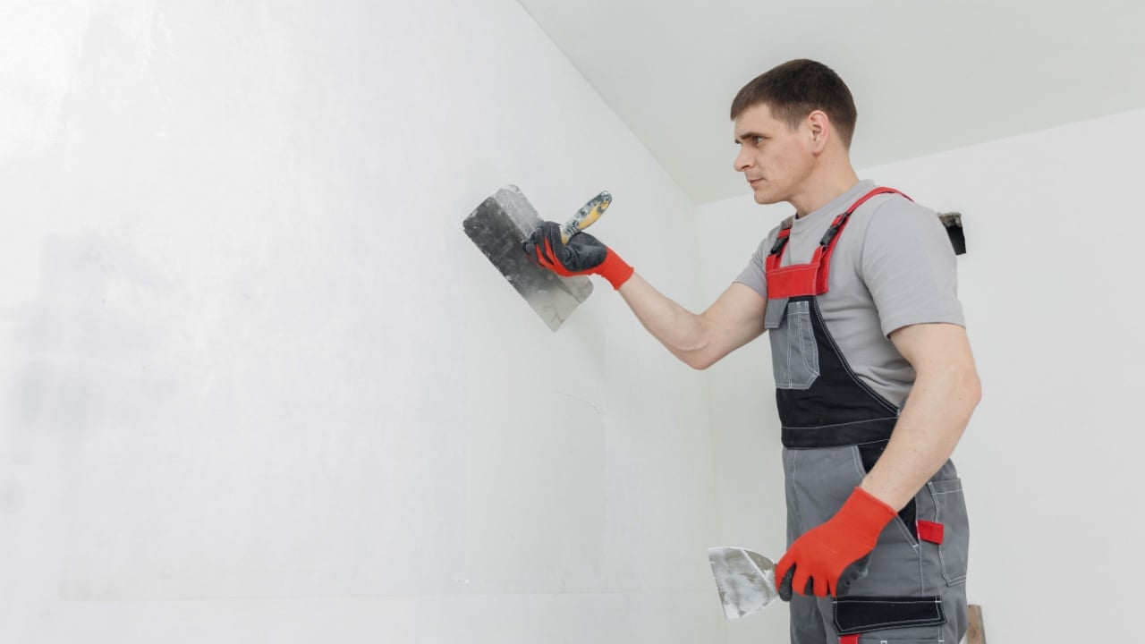 Closeup hands man drywall worker using trowel for plasterer putting stucco on plasterboard white wall.