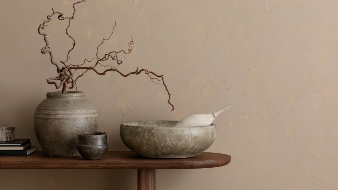 Minimalist composition of living room interior with copy space, wooden consola, ceramic bowl, gray vase with branch, cup, beige wall and personal accessories. Home decor.