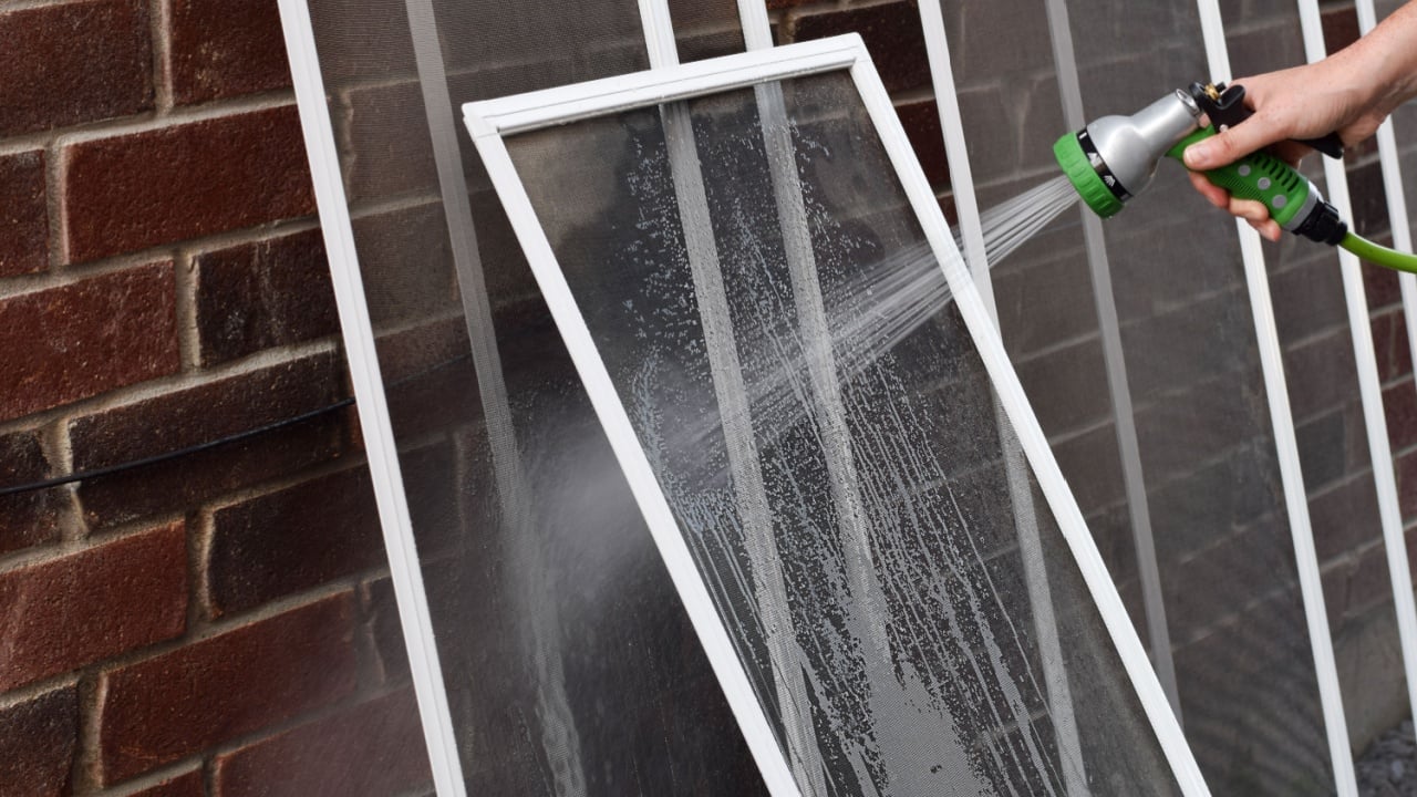 Closeup hand of a person washing dirty window screens with water hose