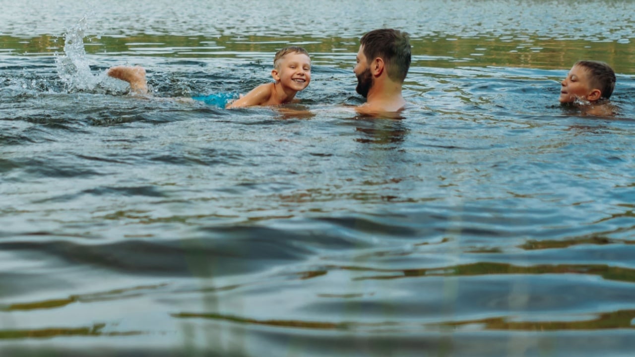 Cheerful funny boy in river wearing goggles for swimming and splashes in rays of sun