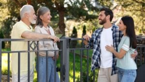 Friendly relationship with neighbours. Young family talking to elderly couple near fence outdoors