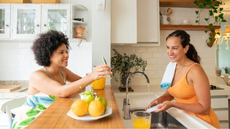happy woman showing mobile screen to friend in the kitchen