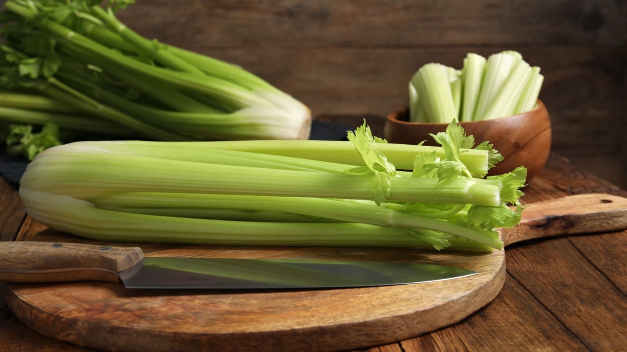 Fresh green celery bunches and knife on wooden table