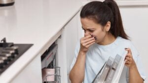 woman smells strange and terrible smell coming from dishwasher machine in kitchen