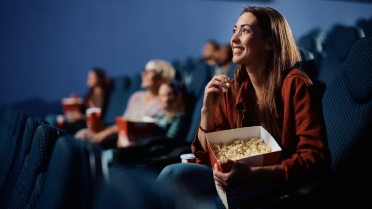 Young woman enjoying in movie projection while eating popcorn in cinema.