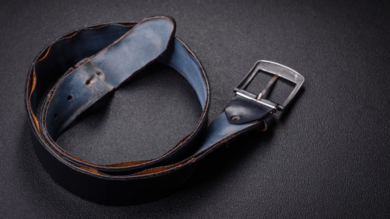 Old leather men's belt with an old-style metal buckle on a dark concrete background