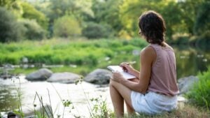 A brunette woman writing near the river