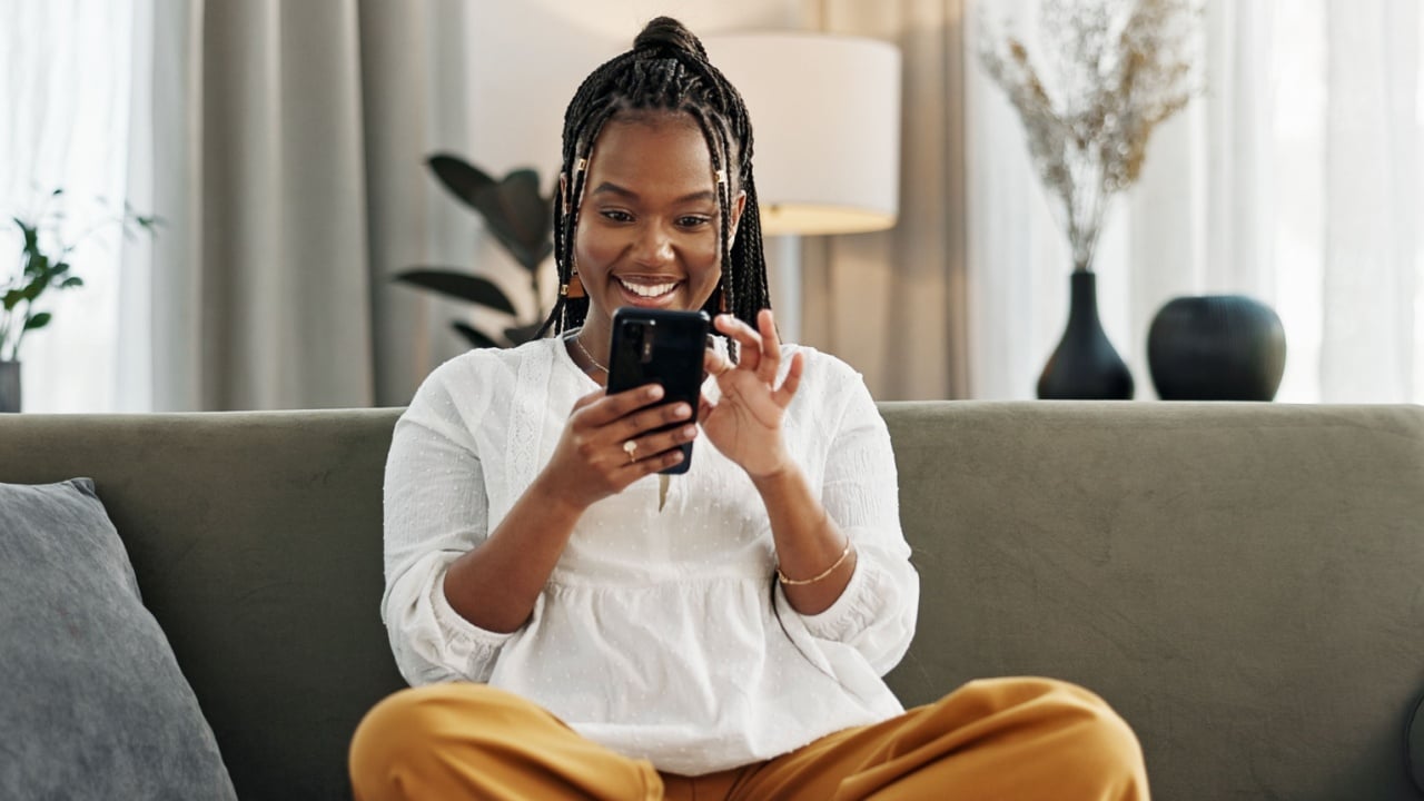 Home, funny and black woman on a sofa, cellphone and connection with social media, comedy post and laugh. African person, apartment or girl on couch, smartphone or mobile user with humor or typing