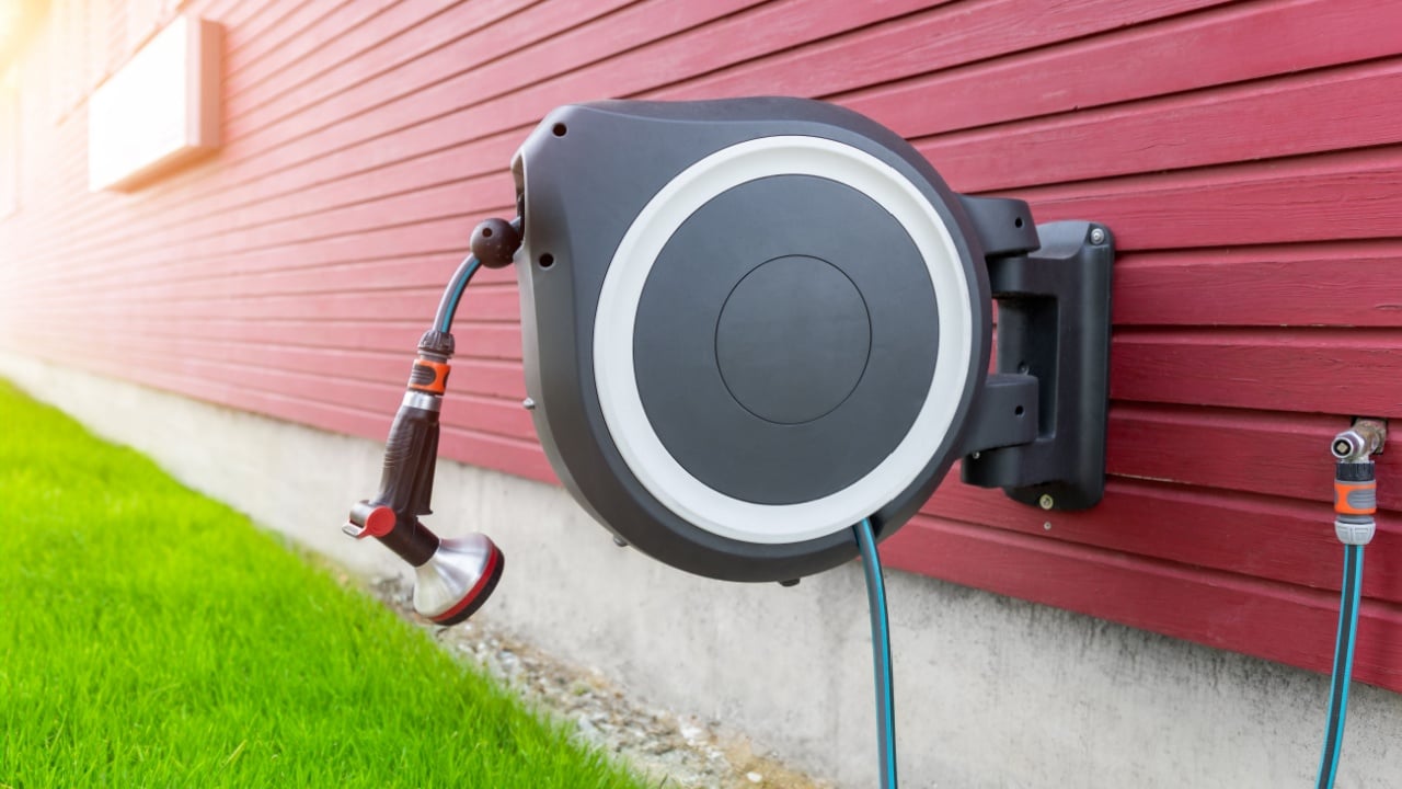 Wall Mounted Retractable Hose Reel. Modern garden lawn watering tip hose with sprinkler hanged at home wall. Lawn and plant tree smart irrigation water system equipment tool