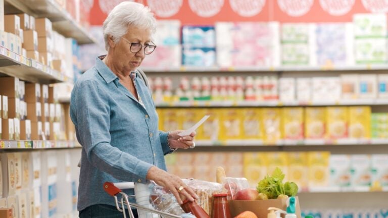 Senior woman checking her grocery list and products in the trolley at the supermarket