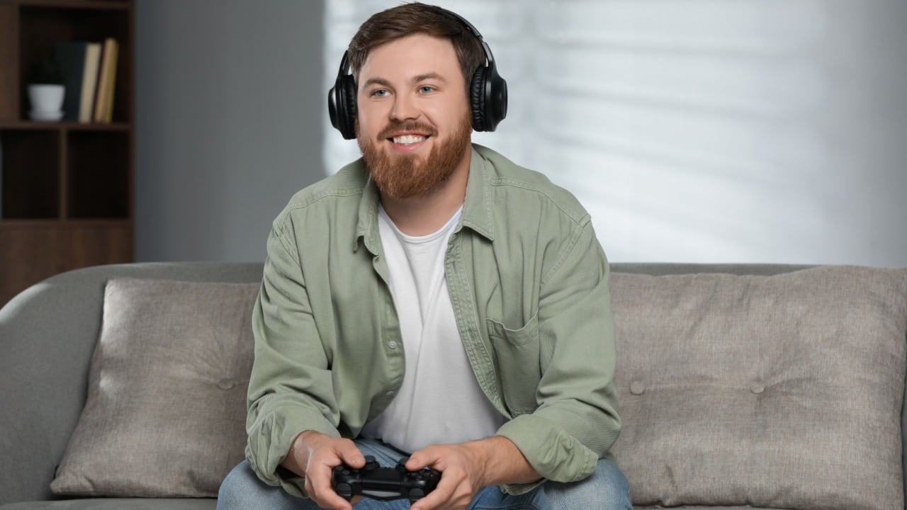 Happy man in headphones playing video game with controller at home