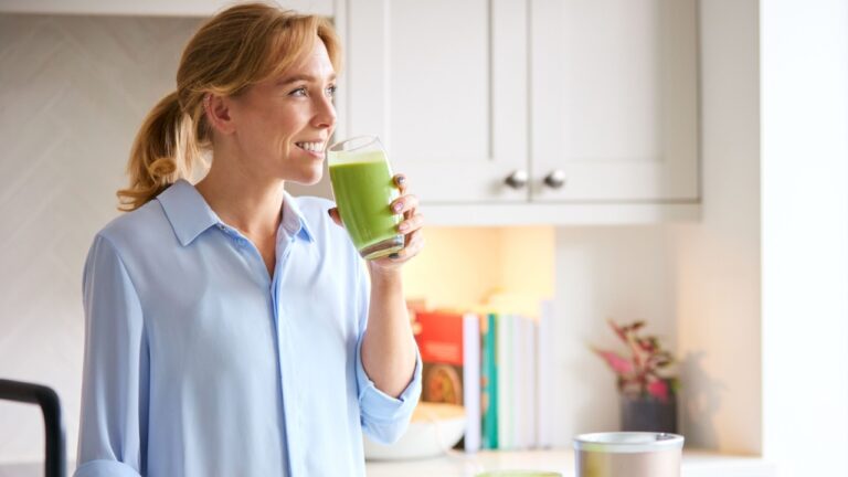 Woman Drinking Fresh Healthy Homemade Smoothie From Glass In Kitchen At Home