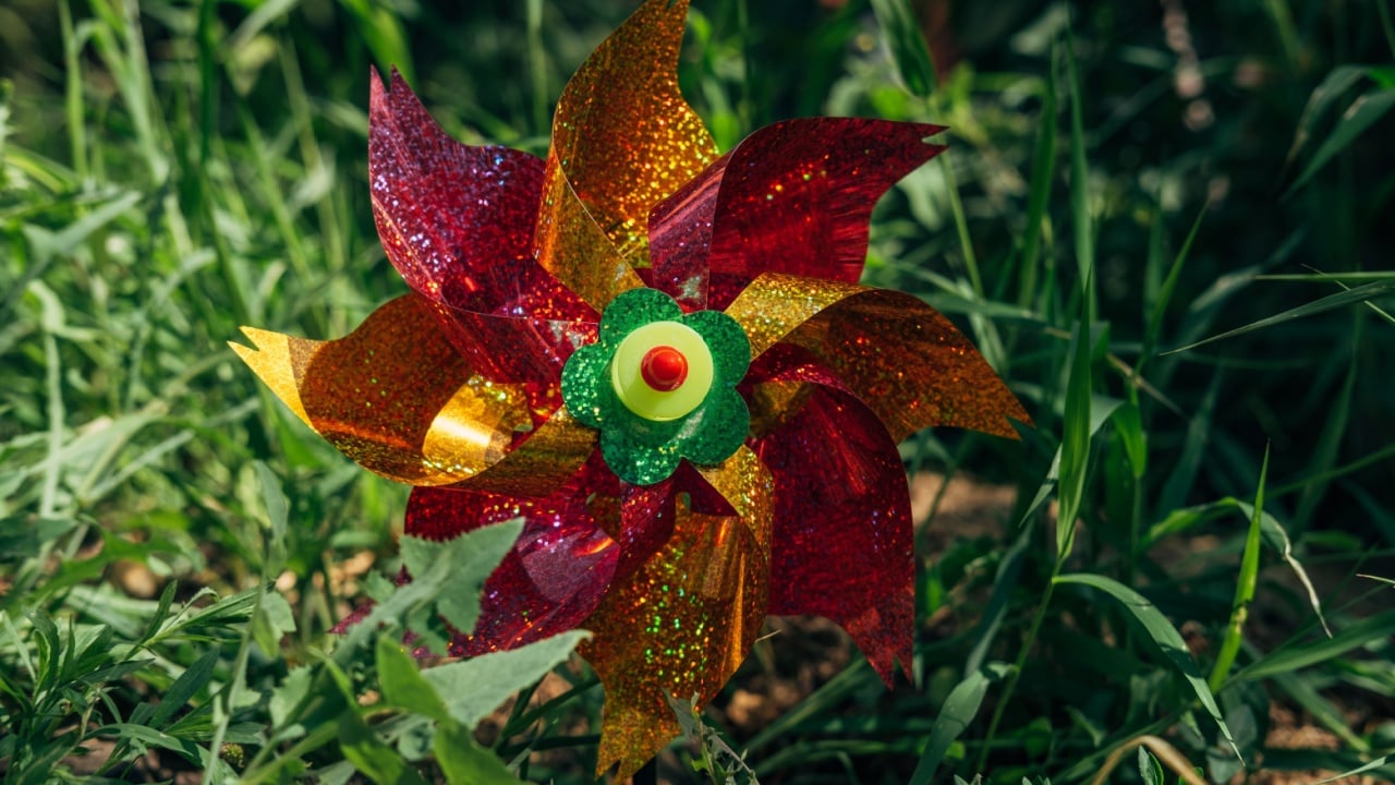 Plastic colorful pinwheel rotating, blowing by wind against the smooth green leaves surface in the garden. Toy windmill. Childhood concept